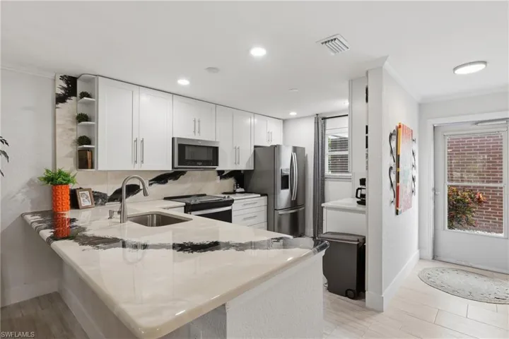 Kitchen featuring white cabinetry, stainless steel appliances, a bar-height counter with integrated sink, recessed lighting, and a patterned backsplash