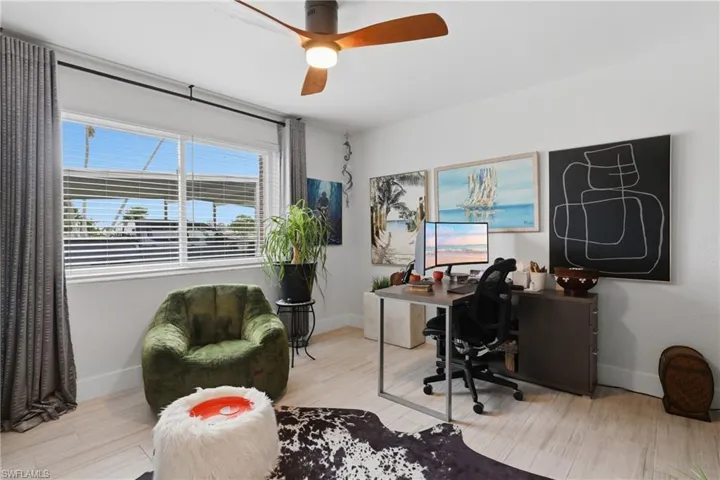 Bright room featuring a large window with horizontal blinds, a modern ceiling fan with wood-finish blades, and light wood-finish flooring