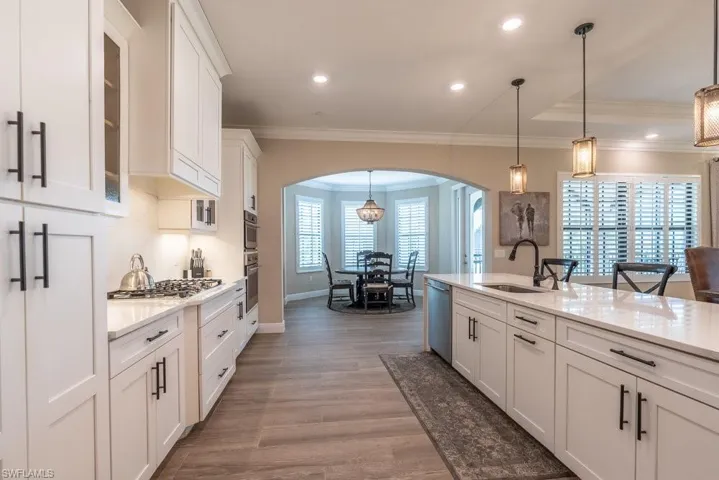 Kitchen with a sink, arched walkways, stainless steel appliances, white cabinetry, and glass insert cabinets