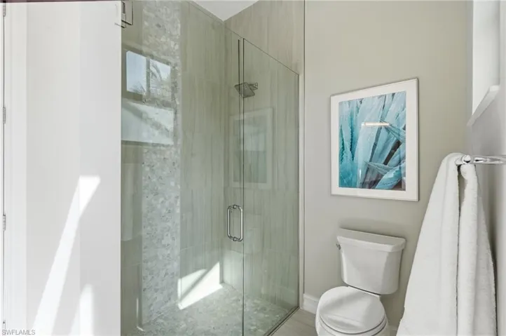 Frameless glass shower enclosure with a rainfall showerhead, tiled walls, and a white toilet