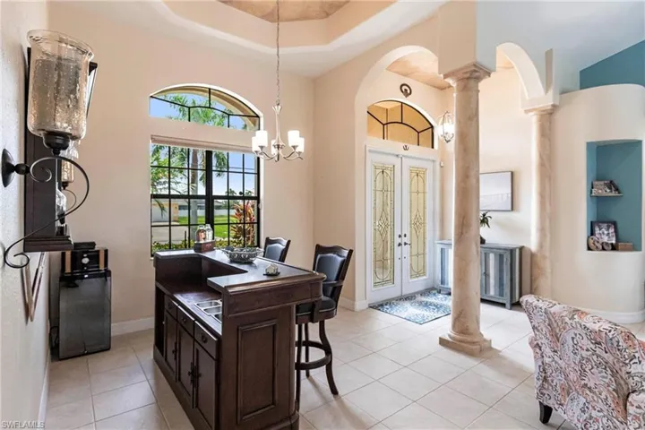 Office space featuring a towering ceiling, ornate columns, a chandelier, light tile flooring, and a raised ceiling