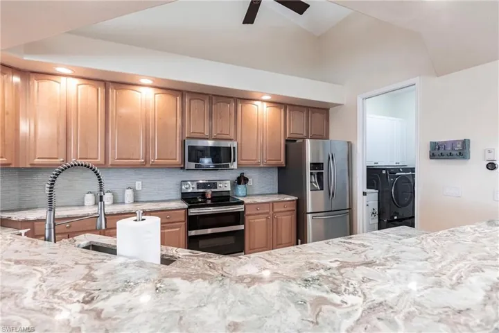 Kitchen with stainless steel appliances, light stone counters, independent washer and dryer, tasteful backsplash, and ceiling fan