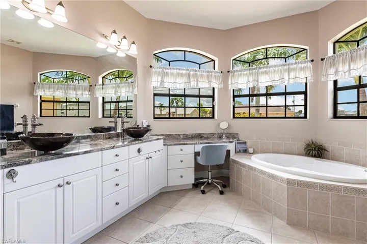 Bathroom with tile floors, tiled tub, and double sink vanity