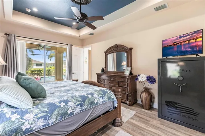 Bedroom with ceiling fan, a tray ceiling, light wood-type flooring, and access to outside
