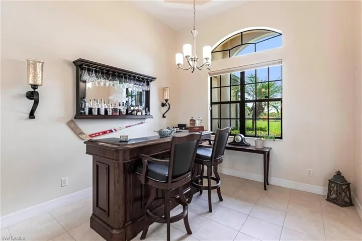 Bar featuring a towering ceiling, an inviting chandelier, decorative light fixtures, and light tile floors