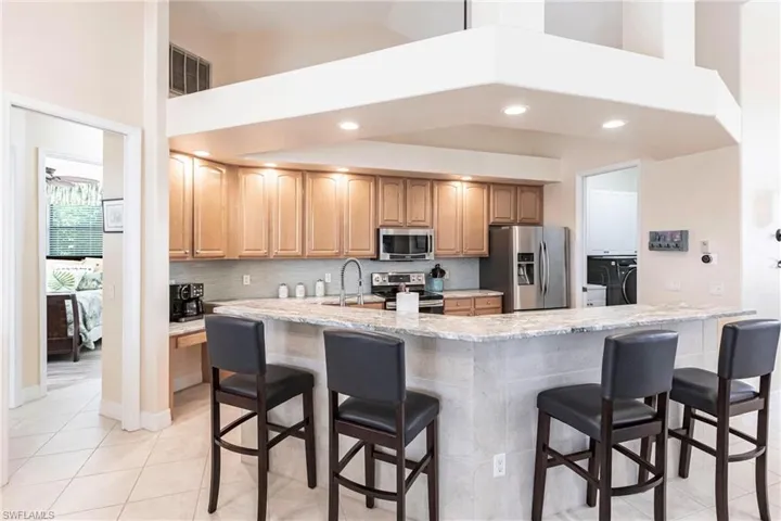 Kitchen with stainless steel appliances, a kitchen bar, high vaulted ceiling, and light stone countertops