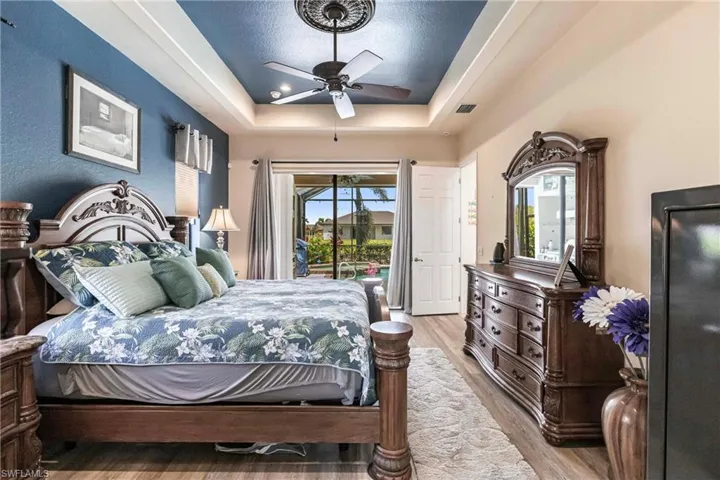 Bedroom with light hardwood / wood-style floors, ceiling fan, a raised ceiling, and access to exterior