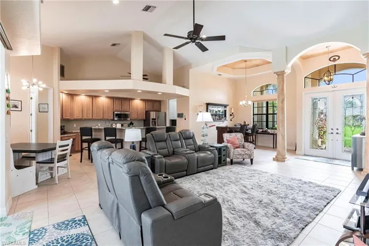 Living room with ceiling fan with notable chandelier, light tile floors, high vaulted ceiling, decorative columns, and french doors