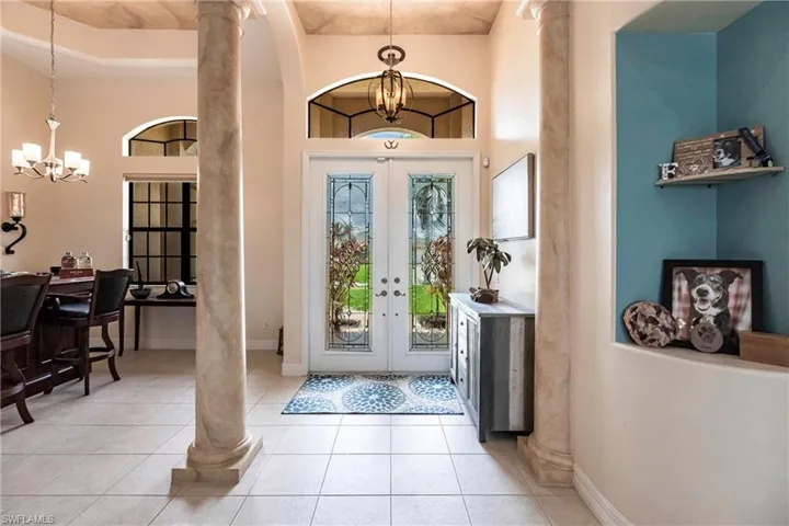 Entrance foyer with an inviting chandelier, a towering ceiling, a raised ceiling, ornate columns, and french doors