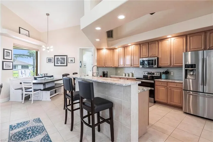 Kitchen featuring stainless steel appliances, light stone counters, hanging light fixtures, a kitchen island with sink, and a chandelier