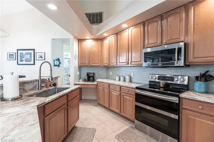 Kitchen featuring light stone countertops, tasteful backsplash, light tile floors, sink, and appliances with stainless steel finishes