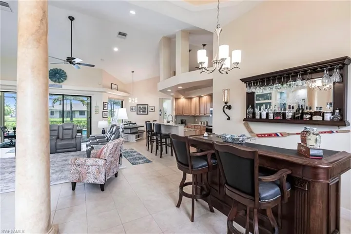 Bar with high vaulted ceiling, ceiling fan with notable chandelier, decorative light fixtures, and light tile floors