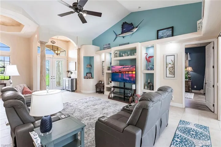 Living room featuring french doors, decorative columns, high vaulted ceiling, light tile flooring, and ceiling fan