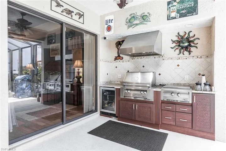 Kitchen with wall chimney range hood, beverage cooler, stovetop, tasteful backsplash, and ceiling fan