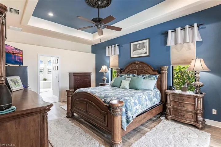 Bedroom with wood-type flooring, connected bathroom, ceiling fan, and a tray ceiling