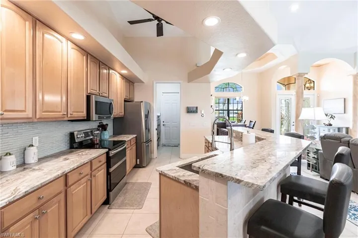 Kitchen featuring light tile flooring, ceiling fan, tasteful backsplash, light stone countertops, and appliances with stainless steel finishes