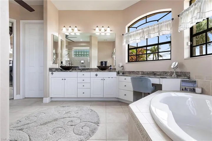 Bathroom with a relaxing tiled bath, dual bowl vanity, ceiling fan, and tile floors