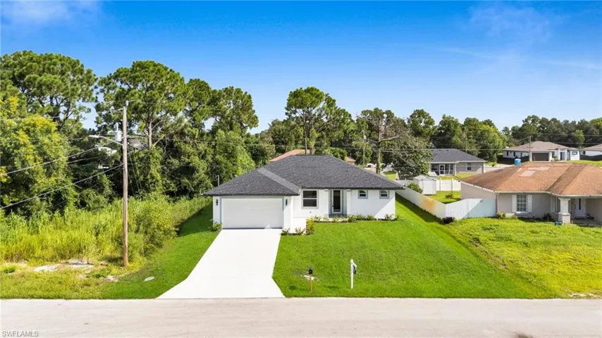 View of front of property with concrete driveway, an attached garage, stucco siding, view of wooded area, and roof with shingles