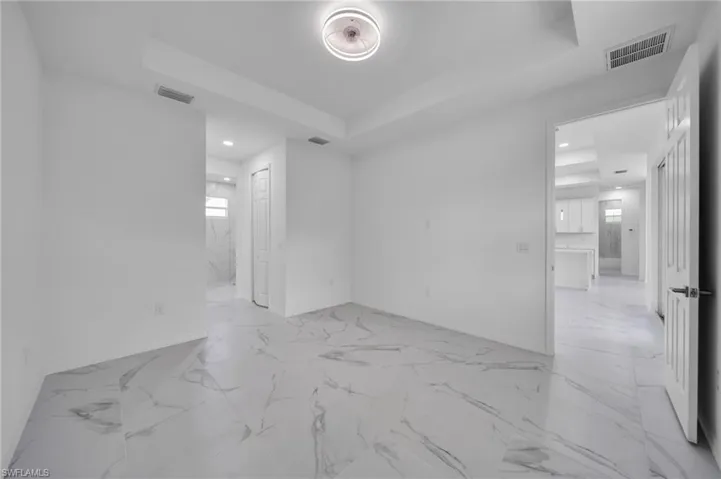Empty room featuring a tray ceiling, recessed lighting, and light marble finish flooring
