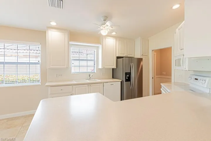 Kitchen featuring light countertops, white appliances, a ceiling fan, recessed lighting, and white cabinets