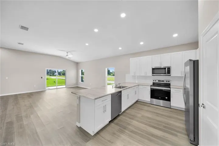Kitchen featuring light hardwood / wood-style floors, white cabinetry, kitchen peninsula, and stainless steel appliances