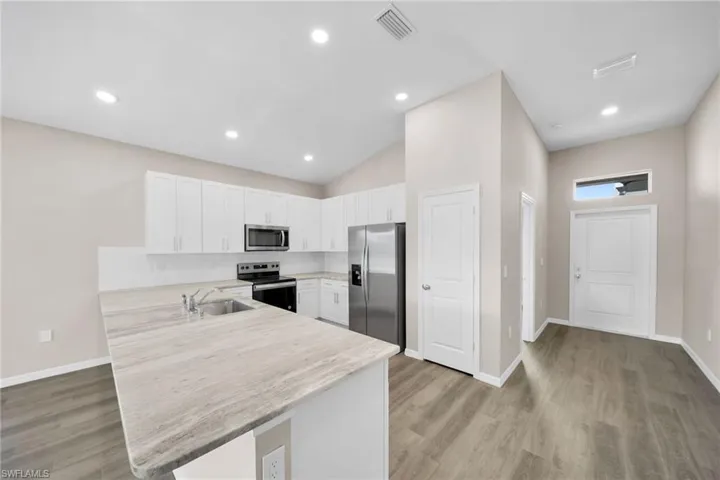 Kitchen with kitchen peninsula, appliances with stainless steel finishes, sink, white cabinets, and light hardwood / wood-style floors