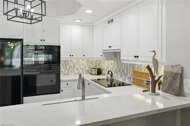 The kitchen features white cabinetry, a built-in oven, a black refrigerator, and a light-colored countertop