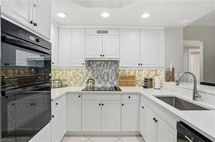 Well-appointed kitchen featuring white cabinetry, integrated oven, a stainless steel sink, and a tiled backsplash