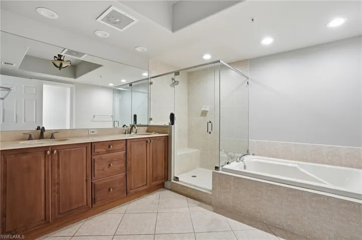The bathroom features a double vanity with a light-colored countertop, a glass-enclosed shower, and a built-in bathtub