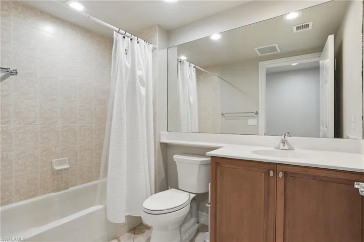 Bathroom featuring a white bathtub, tiled shower walls, a vanity with a white countertop and brown cabinetry, and a large mirror