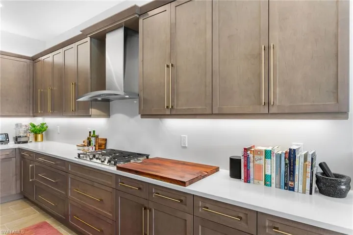 Kitchen featuring wall chimney range hood, stainless steel gas stovetop, and dark brown cabinetry