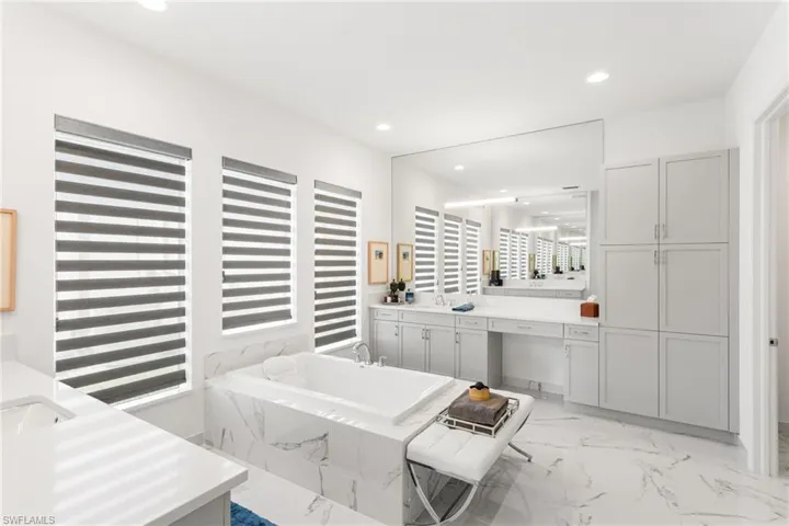 Full bath with vanity, recessed lighting, a tub with marble appearance, and light marble finish floors