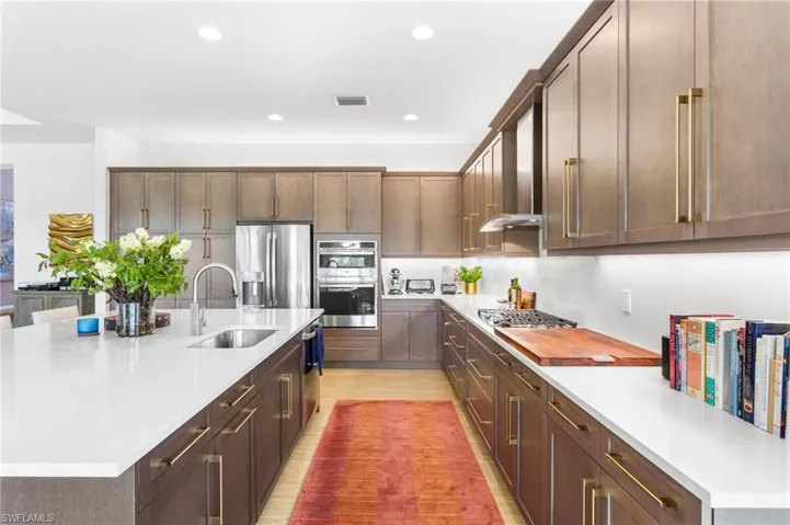 Kitchen with a center island with sink, dark brown cabinetry, appliances with stainless steel finishes, wall chimney exhaust hood, and recessed lighting