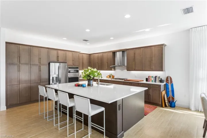 Kitchen with a center island with sink, a kitchen bar, stainless steel appliances, recessed lighting, and wall chimney range hood