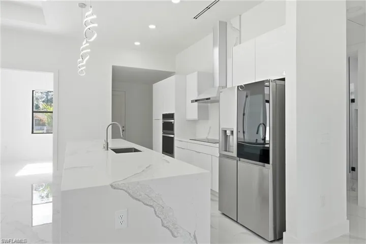 Kitchen featuring a waterfall-edge island with an undermount sink, stainless steel appliances, white cabinetry, and a modern pendant light fixture