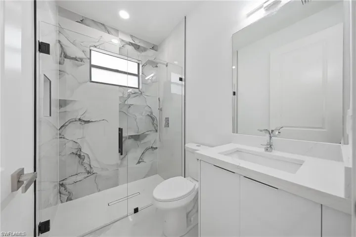 Modern bathroom featuring a frameless glass shower enclosure, large format marble-look tile, a built-in shower niche, a window, and a vanity with an integrated sink