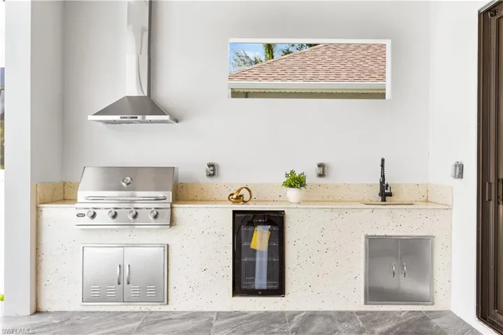 OUTDOOR KITCHEN features BUILT-IN GAS GRILL w/ HOOD VENT, mini-refrigerator, storage & large commercial sink, ideal for OUTDOOR DINING!