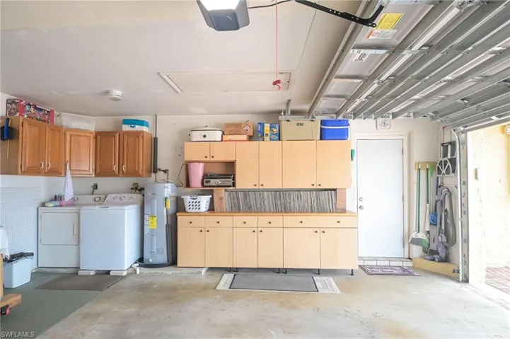 Garage featuring washing machine and clothes dryer, a garage door opener, and water heater