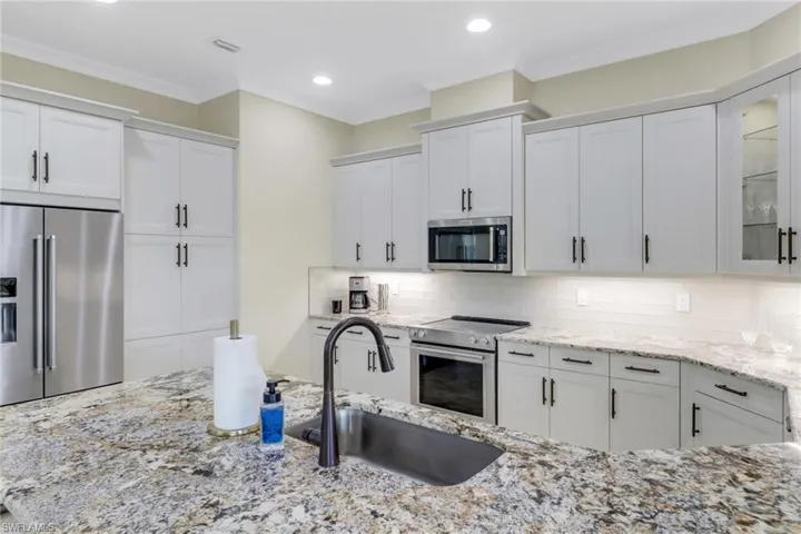 Kitchen featuring appliances with stainless steel finishes, white cabinets, glass insert cabinets, light stone countertops, and crown molding