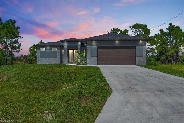 Prairie-style home with driveway, stone siding, a lawn, a garage, and roof with shingles