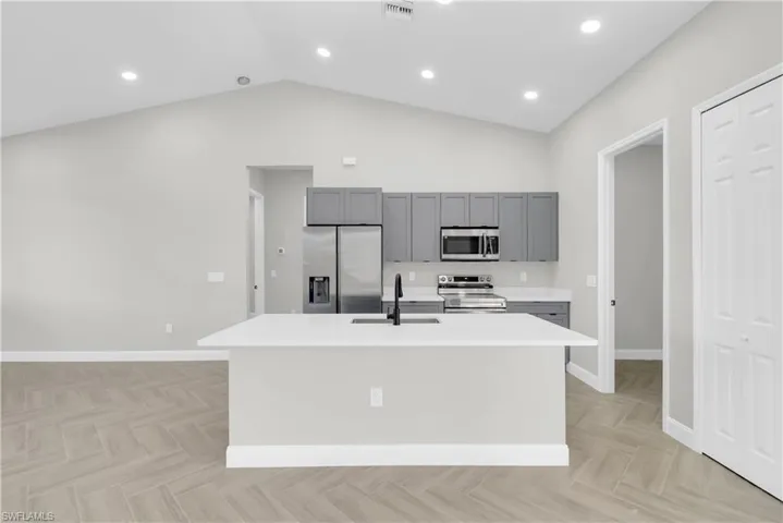 Kitchen featuring appliances with stainless steel finishes, a kitchen island with sink, gray cabinets, vaulted ceiling, and recessed lighting
