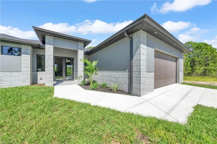View of front of house with stone siding, an attached garage, stucco siding, and a front lawn