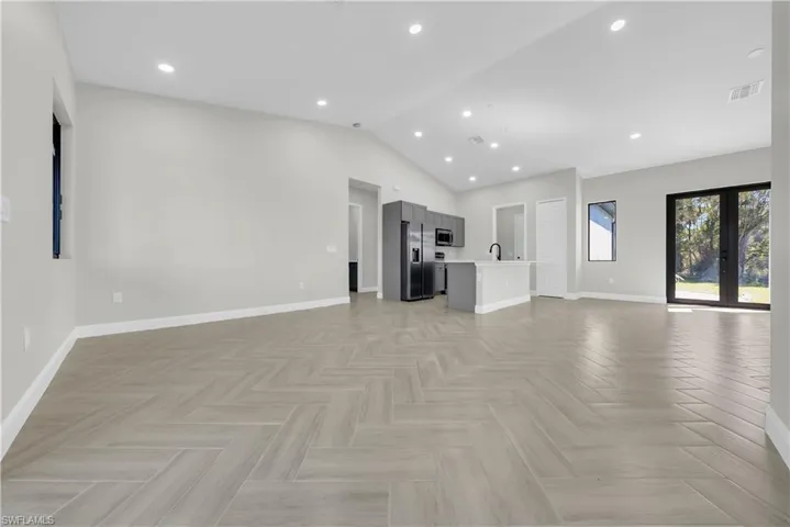 Unfurnished living room with vaulted ceiling, recessed lighting, and french doors