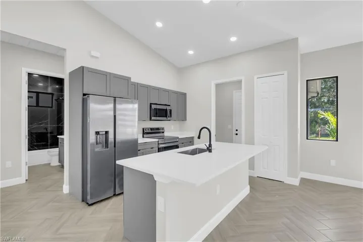 Kitchen with appliances with stainless steel finishes, gray cabinets, an island with sink, recessed lighting, and light stone counters