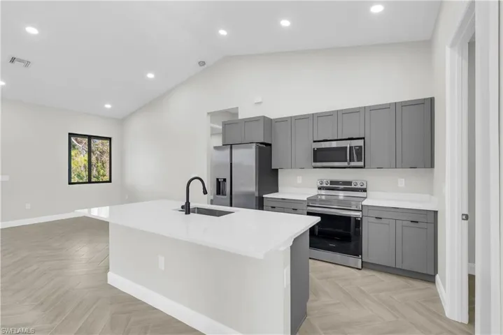 Kitchen with appliances with stainless steel finishes, gray cabinets, a center island with sink, recessed lighting, and light stone countertops
