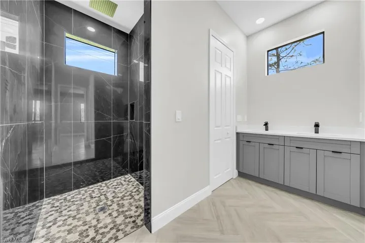 Bathroom with a marble finish shower, double vanity, and recessed lighting