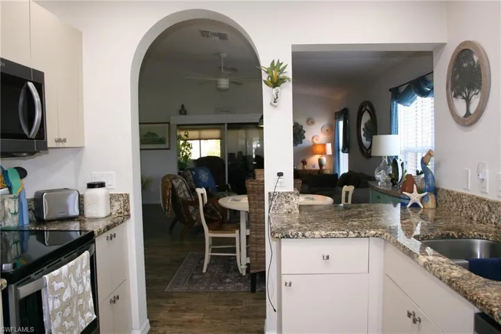Open-concept kitchen and dining area featuring white cabinetry, granite countertops, stainless steel appliances, and an arched entryway with wood-finish flooring throughout