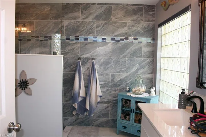 Shower enclosure with grey-patterned tile walls, mosaic tile accent, and glass block window