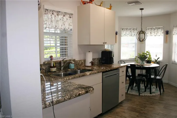 Modern kitchen featuring cream cabinetry, granite-style countertops with waterfall island edge, stainless steel appliances, and wood-finish flooring throughout