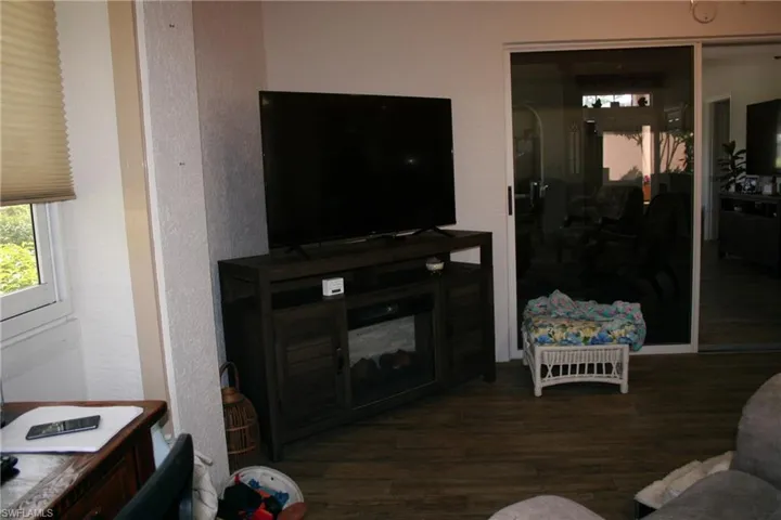 Wood-finish flooring throughout, featuring a window with a cellular shade and a white sliding glass door